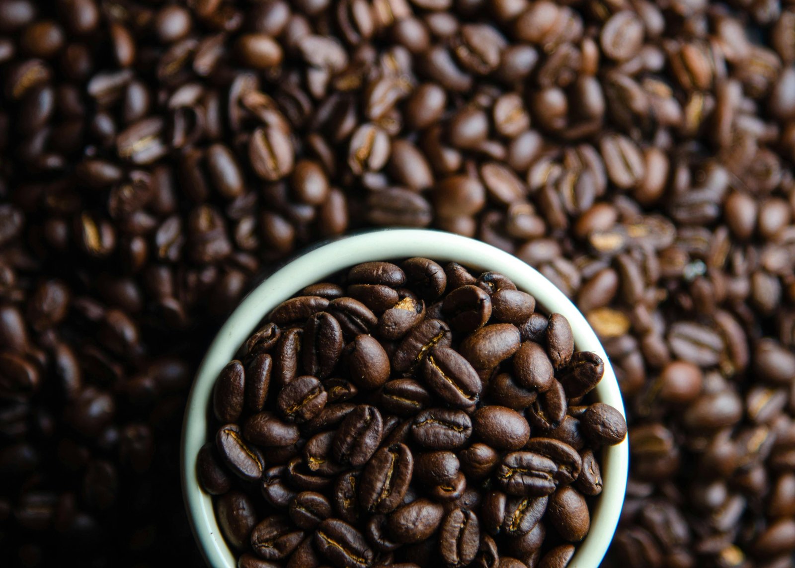 Close-up view of dark roasted coffee beans overflowing from a white mug.
